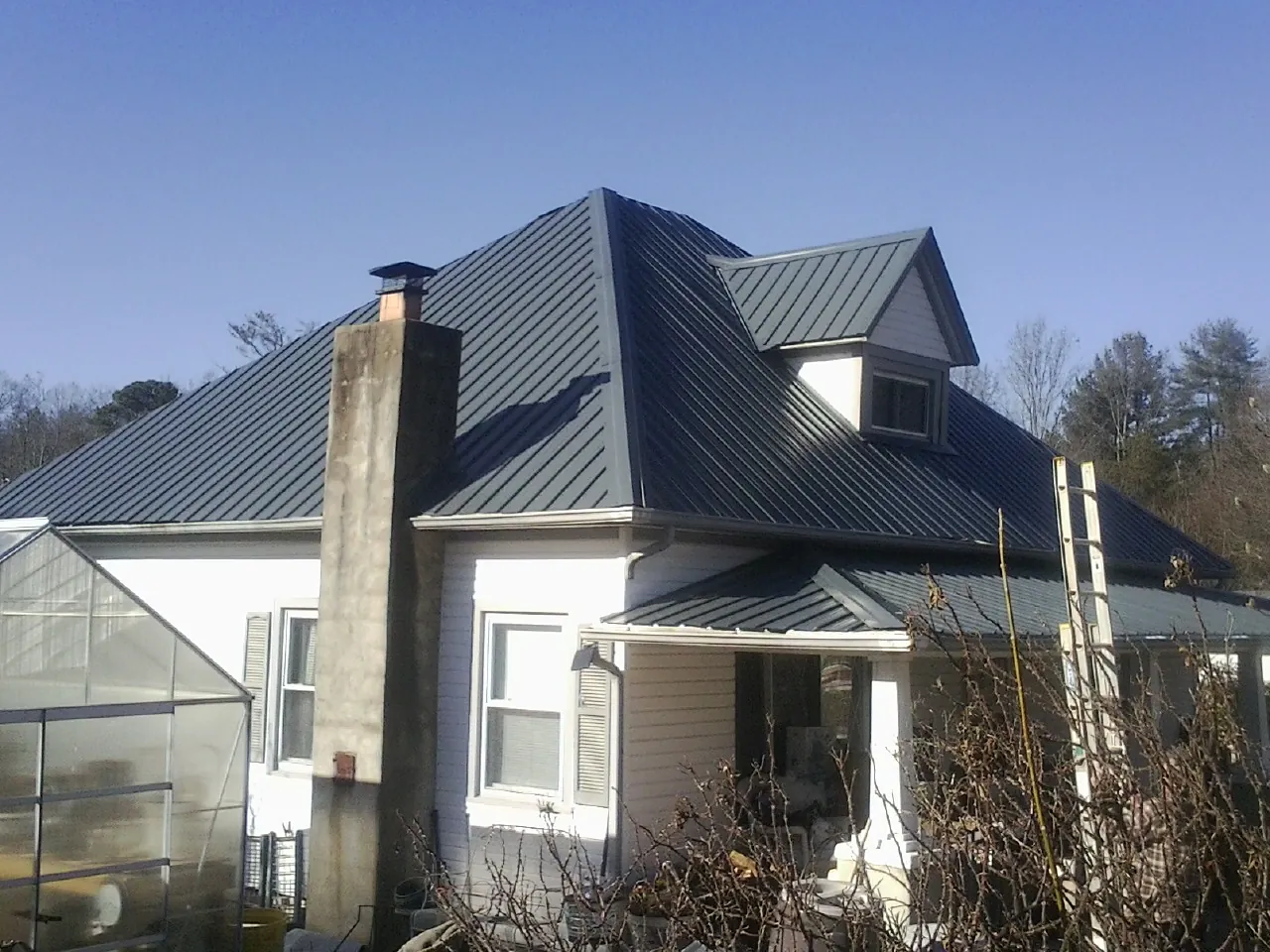 Dark blue standing seam metal roof on a white farmhouse with dormer — Slate & Tile Roof Repair by Roofing Brothers in Blount