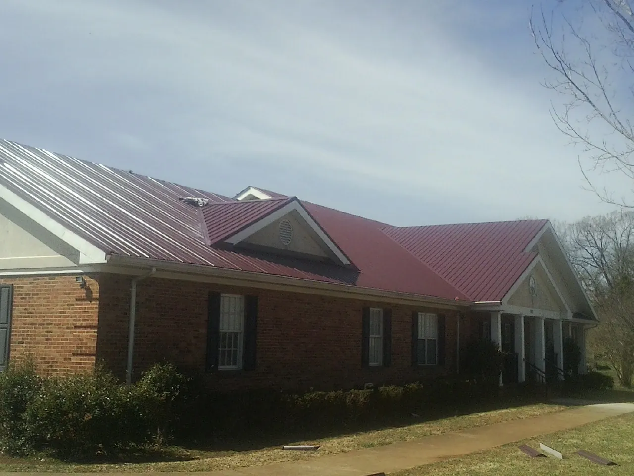 Red metal roof with gabled entries on a long brick building, from a Hail Damage Roof Repair job in Blount