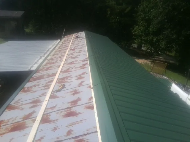 Old rusted panels beside newly installed green metal roofing — Wind Damage Roof Repair by Roofing Brothers in Blount