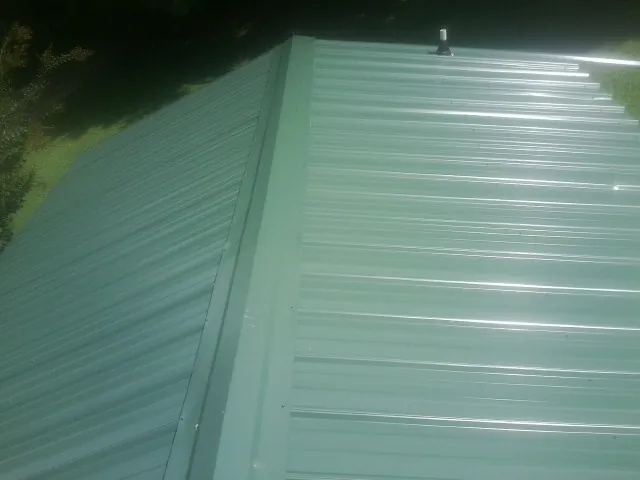 New green metal panels meeting at the ridge of a roof — Flat Roof Repair work by our crew in Blount