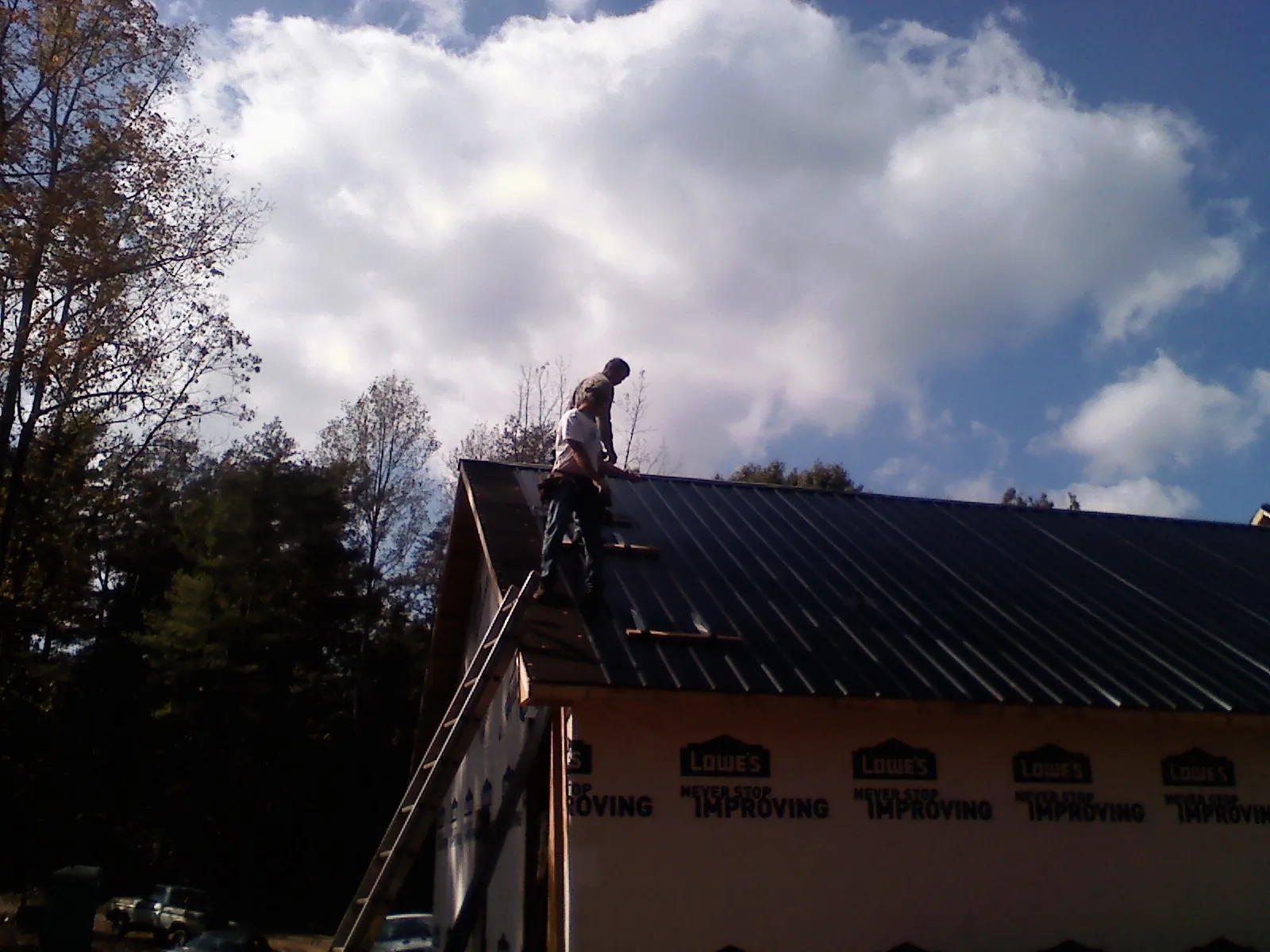 Roofer fastening dark metal panels high against a cloudy sky, from a Roof Inspection job in Blount